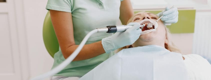 Dental cleaning professional - Unique Dental of Framingham Dental professional in mint scrubs and gloves works inside a patient’s open mouth with dental instruments.