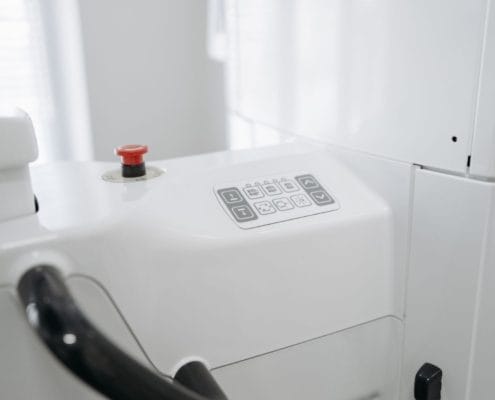 Close-up of a white medical device with a red emergency stop button and control panel.