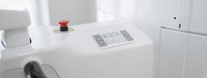 Close-up of a white medical device with a red emergency stop button and control panel.