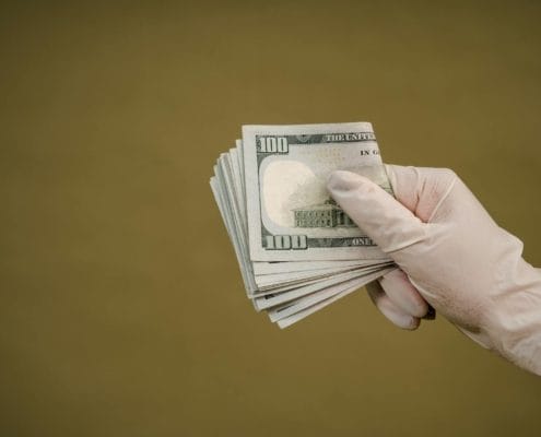 Gloved hand holding a fan of US $100 bills, showing cash in a bundle.
