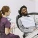 Dentist generations family care - Unique Dental of Framingham Black man reclining in a dental chair, talking with a female dentist in purple scrubs in a clean clinic.