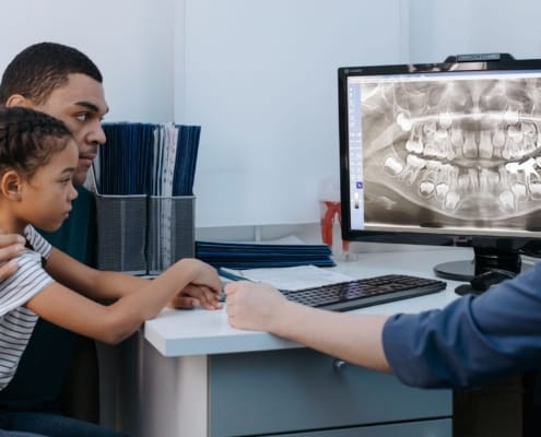 A father and daughter discuss dental care with a dentist reviewing an X-ray.