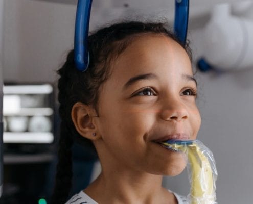 Young girl calmly undergoing a medical imaging procedure with laser alignment lines across her face and blue head support.