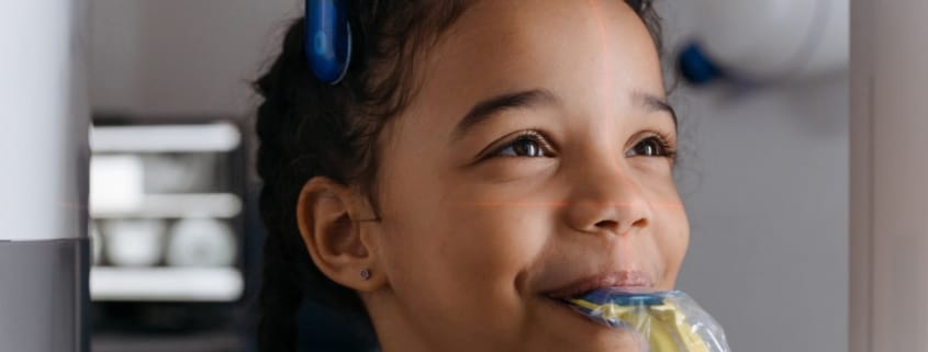 Framingham Family Dentist Keeps Smiles Healthy - Unique Dental of Framingham Young girl calmly undergoing a medical imaging procedure with laser alignment lines across her face and blue head support.