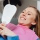 Happy dental visit positive experience - Unique Dental of Framingham Woman reclined in a dental chair wearing a pink bib, smiling while looking at a handheld mirror