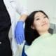 Oral health wellness dental checkup - Unique Dental of Framingham Female patient lying in a dental chair while a clinician in a white coat and blue gloves handles her head.